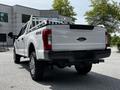 A white 2017 Ford F-250 Super Duty truck with a silver ladder rack on the bed and large off-road tires