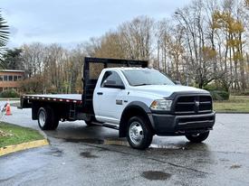 A 2018 RAM 5500 flatbed truck in white with a black bed and grill parked on a wet surface