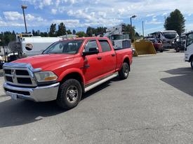 A red 2012 RAM 2500 pickup truck with a crew cab and off-road tires is parked in a commercial area