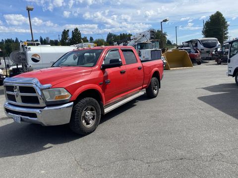 A red 2012 RAM 2500 pickup truck with a crew cab and off-road tires is parked in a commercial area