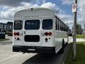 A rear view of a 2022 Blue Bird BB Conventional bus with a white body and red lights displaying the model name "BLUE BIRD" on the back