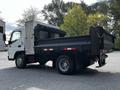 A white 2015 Mitsubishi Fuso FE dump truck with a black dump bed and a small storage compartment in the back parked on a flat surface