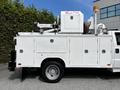 A 2016 Ford F-550 with a white utility bed equipped with various tools and equipment including a mounted generator and a hydraulic arm