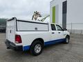 A white and blue 2016 RAM 1500 pickup truck with a truck cap in the bed parked near a construction area