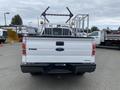 A white 2013 Ford F-150 pickup truck with a ladder rack attached to the bed viewed from the rear