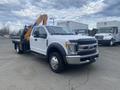 A 2017 Ford F-550 truck with a flatbed and a yellow hydraulic crane attached to the rear