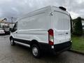 A white 2021 Ford Transit van with a high roof and sliding side door is parked, showcasing its large cargo area and simple design