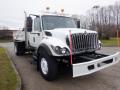 A 2010 International 7300 truck with a white body and black grill visible in the foreground, featuring lights on the roof and an open truck bed