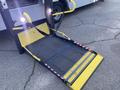 A yellow wheelchair ramp extending from a vehicle with a textured surface and safety markings