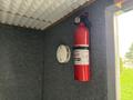 A red fire extinguisher mounted on a wall next to a smoke detector in a gray fabric-covered space