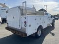 A 2015 Ford F-450 SD with a white utility body featuring storage compartments and a ladder rack on the bed