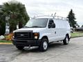 A white 2008 Ford Econoline van with a roof rack and a black grille parked on a paved surface