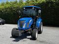 A 2018 New Holland Boomer 45 tractor with a blue body large front wheels and a cab featuring a clear windshield and orange safety light