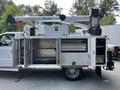 A 2016 Ford F-550 utility truck with an extended cab and mounted aerial work platform featuring open storage compartments on the side