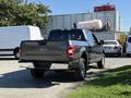 A 2018 Ford F-150 with a gray exterior and chrome accents is parked showing its rear view and large tires