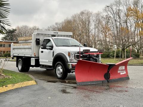 A 2021 Ford F600 truck with a large red snow plow attached to the front and a flatbed at the rear