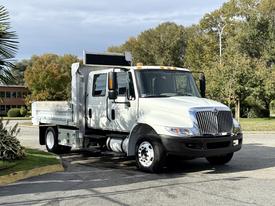 A white 2012 International 4300 truck with a flatbed and side mirrors parked on a road