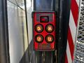 A red and black remote control with four buttons labeled for up and down functions along with power, mounted on a metal surface