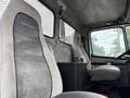 Interior view of a 1998 Freightliner FL80 featuring two gray upholstered seats with the Freightliner logo on the driver's seat and a dark console between the seats