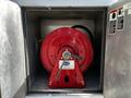 A red hose reel mounted on a metal framework with a manual crank and a visible hose attached