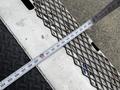 A measuring tape lays across a metal surface with a diamond pattern and a textured black mat in the foreground