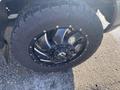 A close-up of a black alloy wheel and tire from a 2000 Ford F-350 SD showcasing deep treads and shiny spokes