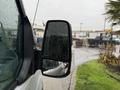 A close-up of a 2019 Ford Transit side mirror covered in raindrops reflecting a blurred view of vehicles and a palm tree in the background