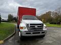 A 2008 Ford F-750 truck with a white cab and chrome grille parked beside a red cargo trailer