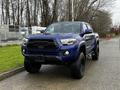 A blue 2022 Toyota Tacoma with a black front grille and large off-road tires parked on a paved surface