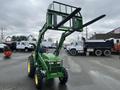 A green 2003 John Deere 790 tractor with a front loader and forklift attachment standing in a parking area