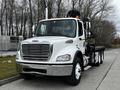 A white 2006 Freightliner M2 112 truck with a chrome grille and multiple lights on the roof, equipped with a flatbed and hydraulic lifting system at the rear