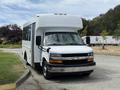 A white 2017 Chevrolet Express partial shuttle bus parked with large windows and a high roof