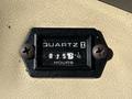 A close-up view of a quartz hour meter displaying 0757 hours with a black casing and two rusted screws on a beige surface