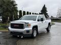 A white 2015 GMC Sierra 1500 pickup truck with a black grille parked on a wet surface with greenery in the background
