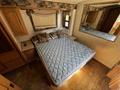 A blue patterned mattress sits atop a wooden bed frame in a motorhome bedroom with decorative pillows against a softly lit wall