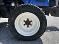 Close-up of a white-rimmed tire on a blue tractor with a rugged tread pattern and visible rust on the wheel hub