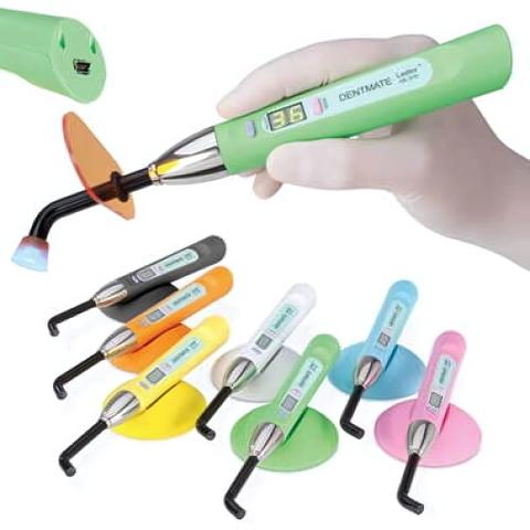 A hand holding a green dental curing light with a digital display surrounded by various colored dental tools and accessories