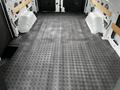 A 2023 Ford Transit van interior showing a clean gray rubber floor with a diamond pattern and wooden supports along the sides