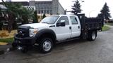 A white 2011 Ford F-550 flatbed truck with dual rear wheels and a black dump bed attached