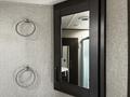 A rectangular mirror with a dark frame is mounted on the wall beside two chrome towel rings in an interior setting