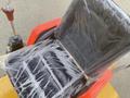 A black seat covered in plastic on a 2024 AGT KRW 23 Mini loader with a red frame and a gear shift visible to the side