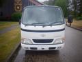 A white 2003 Toyota Toyoace with a flat front design prominent headlights and a black stripe across the grille