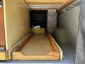 Interior view of a 2017 Mercedes-Benz Sprinter showing a wooden pull-out drawer beneath a storage area with a soft-sided container and a bag