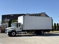 A 2015 Freightliner M2 106 truck with a large white cargo box and black wheels parked on a street
