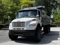 A 2010 Freightliner M2 106 dump truck with a silver body and black accents parked with its bed raised