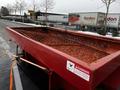 A large red flatbed trailer with a grated surface and safety warning sign, attached to a truck, showing signs of wear and rust
