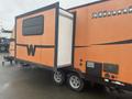 A 2015 Winnebago of Indiana travel trailer with an orange exterior featuring a black stripe and a large slide-out section on one side