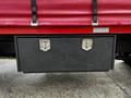 A black storage box with two metal latches attached to the back of a red truck with a tarp cover