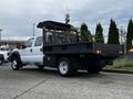 A white 2015 Ford F-550 with a flatbed truck design and a black metal utility body featuring a tool storage compartment and rear lights