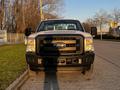 A 2012 Ford F-250 in white with a black front grille and headlights facing forward on a paved road